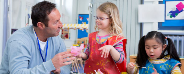 Male teacher talking to one of his nursery students in the classroom.