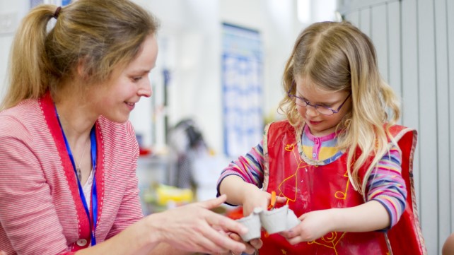 Nursery teacher helping a student cut an egg box in their crafts lesson